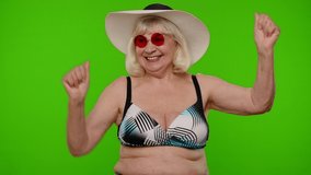 Mature old woman traveler in red sunglasses and hat dancing, celebrating, smiling. Senior grandmother in swimsuit bra on chroma key background. Tourism, summer holiday vacation, trip to sea resort. - Powered by Shutterstock - Get 15% off with code: PIKWIZARD15
