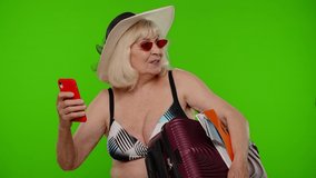 Senior pensioner woman tourist in swimsuit bra taking selfie portrait photo, making video call on mobile phone, chroma key background. Portrait of old granny blogger traveler model on summer vacations
