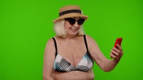 Mature woman traveler blogger in sunglasses, taking selfie on mobile phone, communicating video call online with family. Senior grandmother on chroma key. Tourism, summer holiday vacation, trip to sea