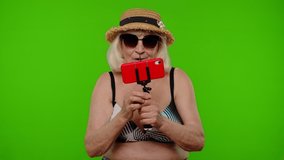 Senior pensioner blogger woman tourist in swimsuit bra talking on mobile cell phone making selfie video call with family, chroma key background. Portrait of granny traveler model on summer vacations