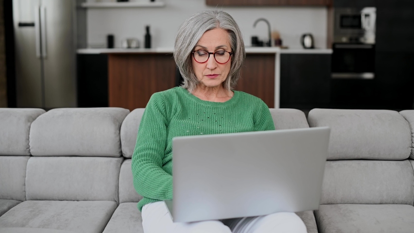 Upset senior woman looks at the laptop screen and feels frustrated, win in lottery, has a problem with job. A mature retired lady receive a bad news or can not afford bills Royalty-Free Stock Footage #1068389183