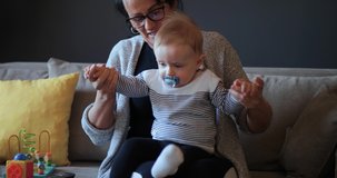 Young grandmother plays with a baby grandson in the living room while a mother broadcasts a live conference