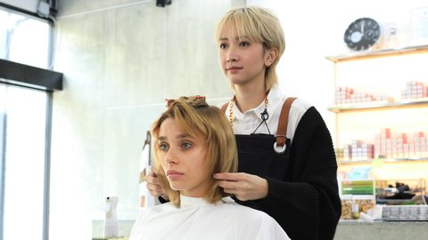 Professional hair dresser trimming, cutting beautiful young woman's hair in modern beauty salon.