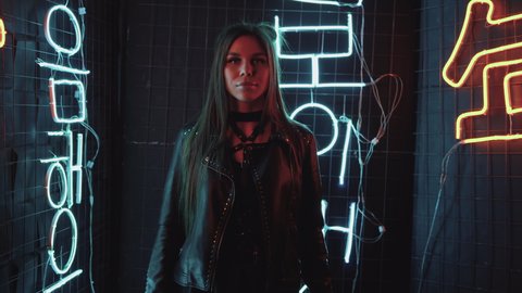 Stylish brunette girl in a leather jacket dances against the wall with light. Fashionable woman dancing single in the club. A hot girl with long hair is performing a modern dance. 4K footage