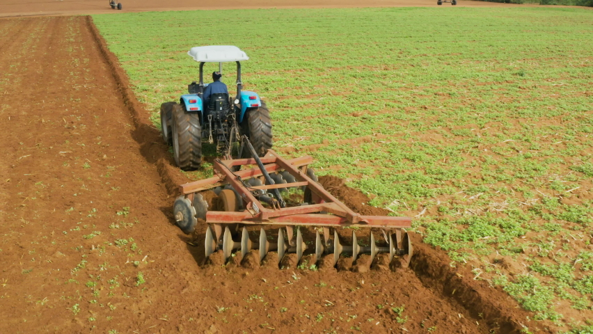 Aerial view of a tractor plowing fields with a rotary plow on a large scale vegetable farm.  Ploughing contributes to climate change and global warming  Royalty-Free Stock Footage #1068393818