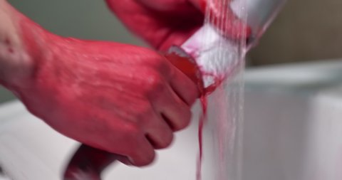 Hand washing. Man wash red bloody hands and violent sharp knife in bath under the water jet. Red water goes in white sink making a scary view.