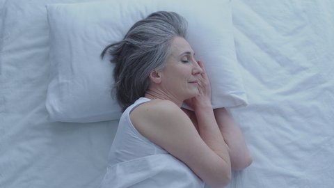 Pretty greyhaired woman sleeping on pillow in the morning, healthy habits, rest