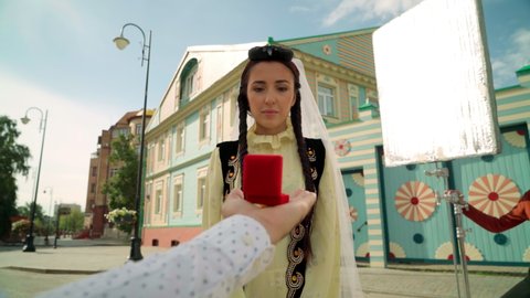 KAZAN, TATARSTAN RUSSIA - AUGUST 23 2020: Pretty surprised young woman in traditional Tatar clothes receives proposal from boyfriend on sunny city street on August 23 in Kazan