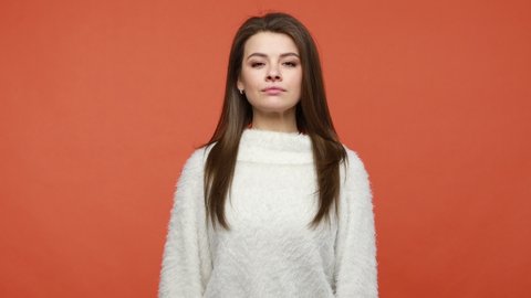 Yes sir! Serious brunette woman in white sweater saluting holding hand near head looking at camera with serious concentrated expression, subordination. Indoor studio shot isolated on orange background