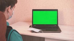A man puts on a protective face mask himself and on the interlocutor by video call and starts typing on a laptop, epidemiological safety, remote work, green screen