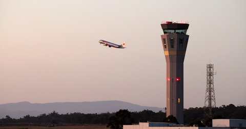 Melbourne, Australia - January 23, 2021: Air Traffic Control Tower at Melbourne Airport with a Jetstar Airbus A320 taking off in the background at dusk.