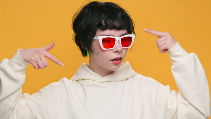 Crazy Shocked Teenager Face Girl Showing Emotion Think About it Really Gesture with Index Fingers to Temple of Head in Sunglasses on Yellow Background. Fashion. Monotone. Emotions People. Lifestyle.  Royalty-Free Stock Footage #1068407003