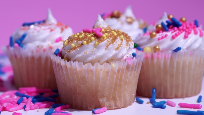 Cupcakes macro shallow depth of field view. Decorated sugar sprinkles cup cakes with white vanilla cream on pink background. Delicious desserts muffins for girl birthday or Valentine day.
