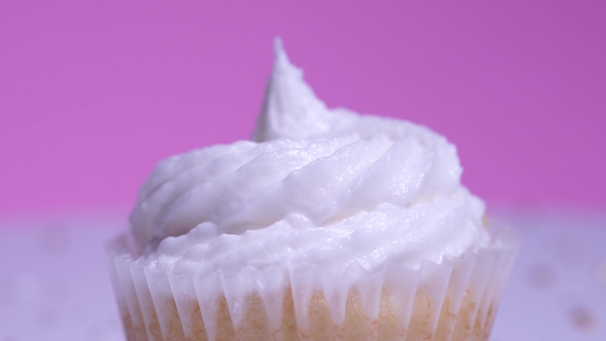 Cupcake macro shallow depth of field view. Decorated sugar sprinkles cup cake with white vanilla cream on pink background. Delicious desserts muffin for girl birthday or Valentine day.