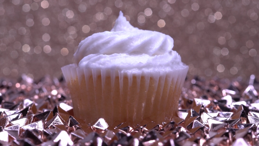 Cute cupcake macro shallow depth of field view. Decoration with sugar sprinkles. Cup cake with white vanilla cream on gold background. Making delicious desserts muffin for birthday or Valentine.