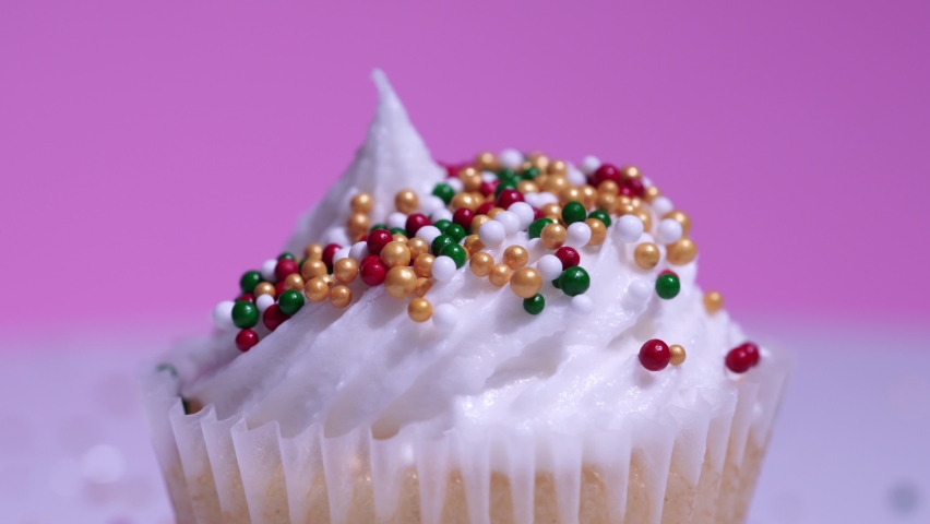 Cute cupcake macro close up, shallow depth of field. Decoration with sugar sprinkles. Cup cake with white vanilla cream on pink background. Delicious surprise desserts muffin for birthday, Valentine.