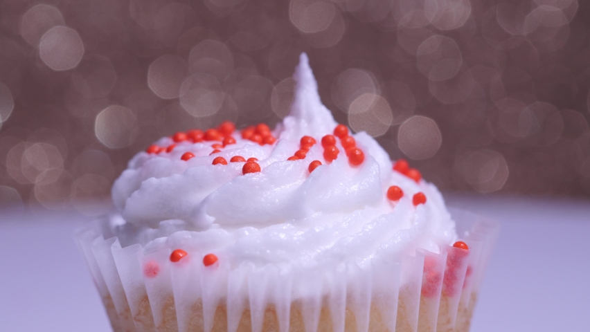 Cute cupcake macro shallow depth of field view. Delicious desserts muffin for girl birthday or Valentine day. Decorated sugar sprinkles cup cake with white vanilla cream on gold background.