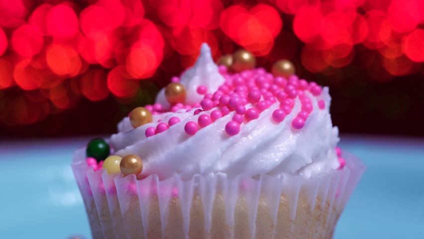 Cute cupcake macro close up, shallow depth of field. Decoration with sugar sprinkles. Cup cake with white vanilla cream on red background. Delicious surprise desserts muffin for birthday, Valentine. 