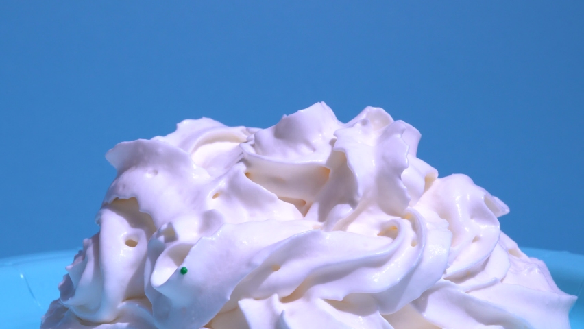 Pouring a bowl of dessert sprinkles at homemade whipped cream. Colourful icing falling on sweet cream, blue background, decoration for cake and bakery, , candy chocolate on frost.