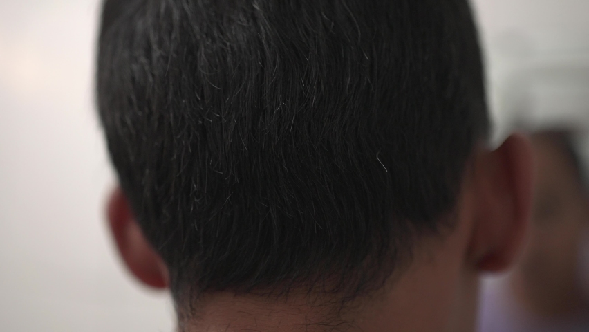 young guy cuts hair himself with shaver in front of the mirror