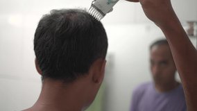 young guy cuts hair himself with shaver in front of the mirror