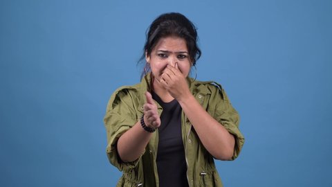 Repulsion to bad smell. Asian girl grabbing nose with fingers, holding breath to avoid stink, awful fart gases, intolerable odor, woman showing stop gesture. studio shot isolated on blue background.
