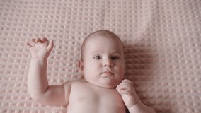 Top view of a cute newborn baby lying on his back on the bed looking at the camera. Close-up portrait of a beautiful Caucasian child. Slow motion 4K video