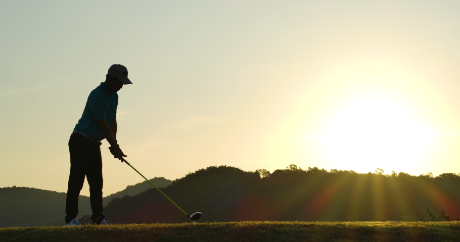 Slow Motion Golf Swing Drive Shot. Silhouette Asian male golfer enjoying vacation luxury resort using driver to tee off golf course fairway over sunset background. Royalty-Free Stock Footage #1068425240
