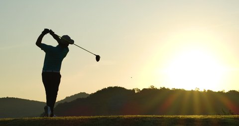 Slow Motion Golf Swing Drive Shot. Silhouette Asian male golfer enjoying vacation luxury resort using driver to tee off golf course fairway over sunset background.
