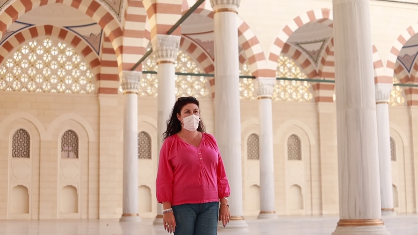 A brunette tourist woman in a protective mask walks through the old mosque in Istanbul on a sunny day.