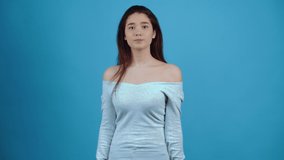 Shy young woman, touches her hair with her hand and smiles shyly. Asian with dark hair, dressed in a blue blouse, isolated on a dark blue background in the studio. Lifestyle concept. Portraits with