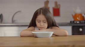 Breakfast in the kitchen. Little girl who doesn't like healthy milk granola in bowl and plays with them. Cute little girl is having breakfast. Slow motion video.