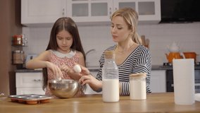 Cute kid girl learning to cook with loving happy mother. Help her cute daughter prepare cookies and bake cakes from her mom in the kitchen. The concept of having fun together.Slow motion video.