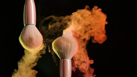 Two makeup brushes, touching each other, form a beautiful multicolored vortex of particles of cosmetic powder. Close up of makeup brushes in dark studio in neon light. Slow motion.