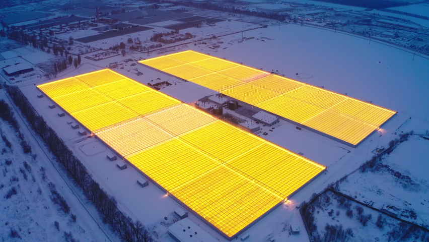 Aerial side view of large industrial greenhouses for growing plants in winter. light pollution. winter day at sunset. Flying along modern plantation glasshouse area. growing plants vegetables flowers Royalty-Free Stock Footage #1068442748