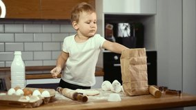 Child boy prepares in the kitchen alone. Kid rolls out the dough with a rolling pin. Independence. Help mom with household chores.