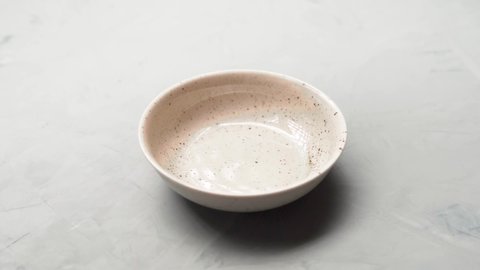Dry cat food slowly falls into a plate on a gray surface