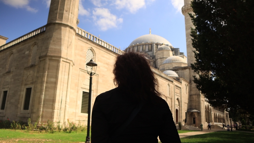 A brunette tourist woman in a protective mask walks through the old mosque in Istanbul on a sunny day.