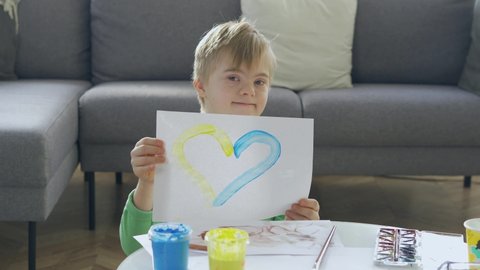 Boy with Down Syndrome holding a picture with yellow and blue heart. Ukraine