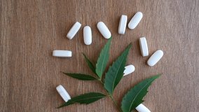 White pills with green  Neem leaf on wooden  table background. Top view. Slow motion video