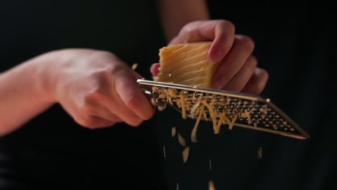 The housewife uses kitchen tools for cooking. She prepares a delicious pizza and rubs hard cheese on a straight iron grater. Close up