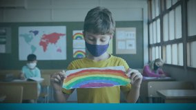 Animation of covid 19 text over schoolboy in face mask holding rainbow drawing. global covid 19 pandemic, education and learning concept digitally generated video. - Powered by Shutterstock - Get 15% off with code: PIKWIZARD15