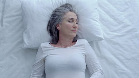 Attractive greyhaired woman waking up in the morning, feeling tired, depression