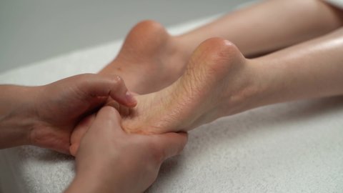 Close-up hands of male masseur massaging feet and toes to young woman lying on massage table in spa salon. Professional physiotherapist with strong hands performing foot massage, closeup.