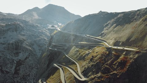 Aerial shot of the top of Stelvio Pass with hairpin corners on a sunny day. Highest paved mountain road in the Eastern Alps. Cars, motorcycles, and bikers are enjoying the ride.