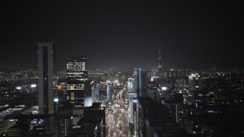 Camera moving up high between modern skyscrapers showing beautiful panorama of Seoul Gangnam District on the night, and then getting lower and flying above busy road street with a lot of traffic. Royalty-Free Stock Footage #1068463739