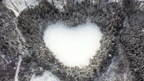 Heart shaped lake in winter forest. Tilting drone shot of natural snow wonder nature environment. Love peace save our planet symbol sign in Swedish woods. frozen pond water special shape Sweden