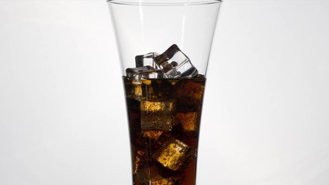 Self pouring cola to the glass with ice in slide movement on white background, stop motion