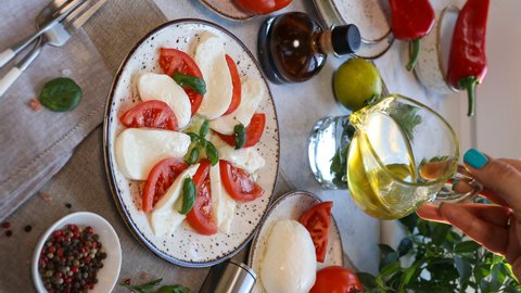 Cinemagraph of Pouring olive oil over caprese salad. Italian caprese salad with Mozzarella cheese. Healthy food and vegetarian concept.  Vertical format.