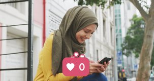 Animation of heart icons and rising number with woman wearing hijab using smartphone in street. global communication technology digital interface concept digitally generated video.